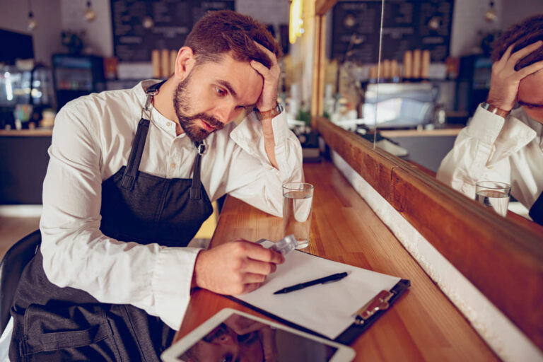 tired-male-barista-with-pills-sitting-at-wooden-co-2026-03-24-23-53-25-utc